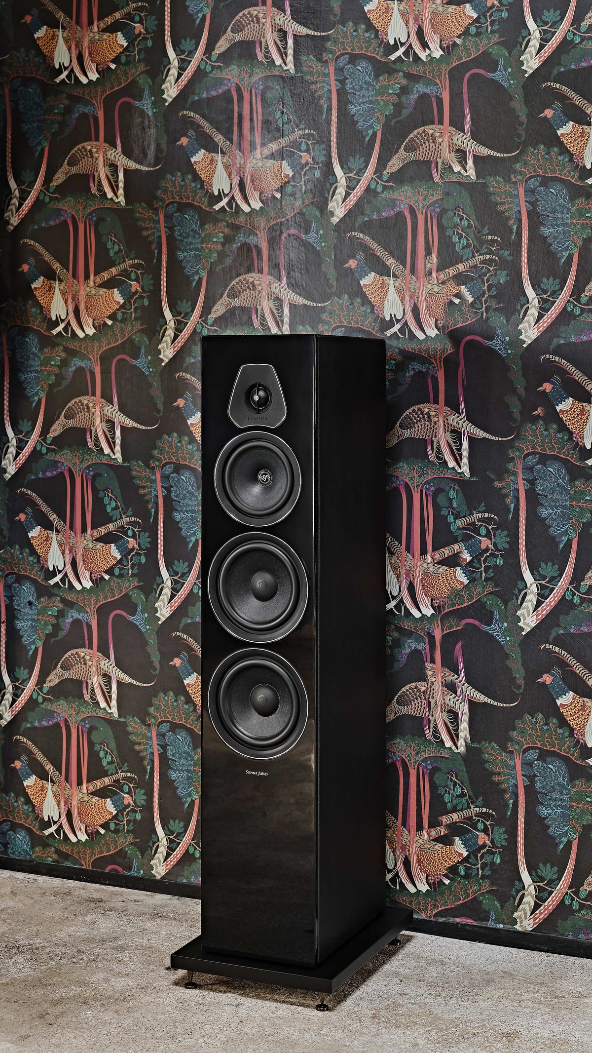 Close-up of the Sonus faber Lumina V floorstanding speaker in sleek piano black, set against a vibrant home wallpaper.