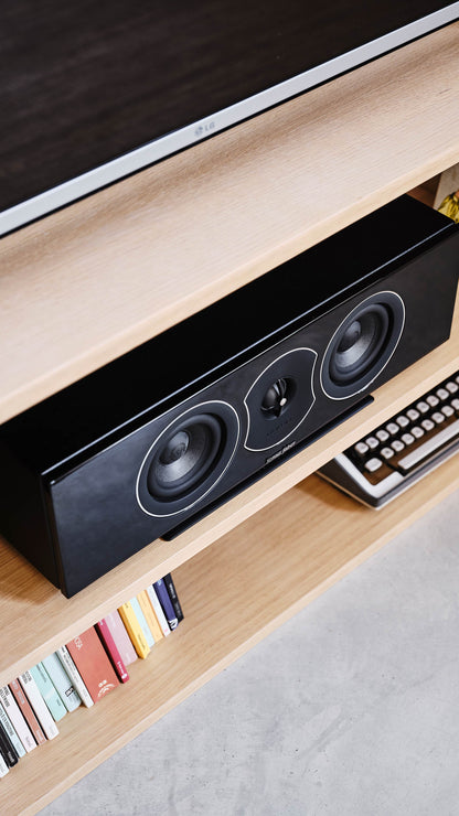 Sonus faber Lumina CI center speaker in stylish piano black lacquer, elevating a home cinema experience on a sleek TV stand.