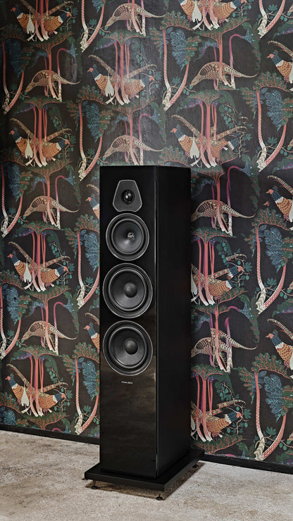 Close-up of the Sonus faber Lumina V floorstanding speaker in sleek piano black, set against a vibrant home wallpaper.
